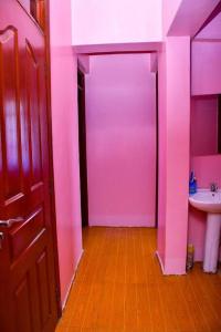 ein rosafarbenes Bad mit einem Waschbecken und einer Tür in der Unterkunft Cozier Domicile Apartments in Maragoli