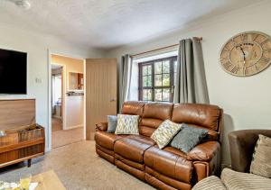 a living room with a brown leather couch and a clock at Chestnut Cottage - Stackpole in Stackpole Elidor