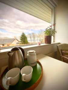 a tray with a tea pot and cups on a table with a window at Værelse med udsigt over Limfjorden - rolige omgivelser og adgang til flot have in Nykøbing Mors