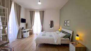 a white bedroom with a bed and a desk and window at Fortuna Guest House in Siracusa