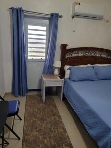 a bedroom with a bed and a window with blue curtains at Sky Blue Residence in Lower Princeʼs Quarter