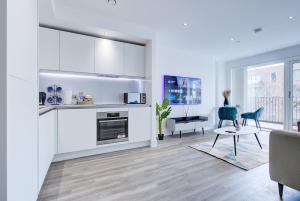 uma cozinha com armários brancos e uma sala de estar com uma mesa em Luxe Apartment by Excel em Londres