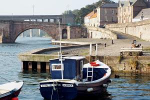 a small boat sitting in the water near a bridge at Mill Wharf in Berwick-Upon-Tweed
