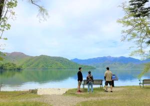 three people standing around a bench near a lake at Hatago Nagomi in Nikko