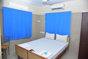 a small room with a bed with blue curtains at SGRT Residency in Vellore