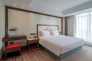 a bedroom with a large white bed and a desk at Suning Universal Hotel ALL-SUITES in Nanjing