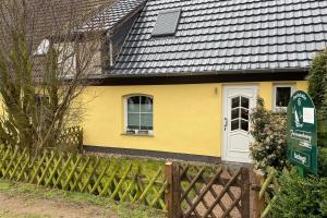 une maison jaune avec une porte blanche et une clôture dans l'établissement Ferienhaus Hinter-Bollhagen, à Wittenbeck