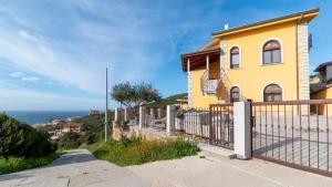 uma casa amarela numa colina com uma cerca em La Rosa dei Venti-Panoramic View em S'archittu Cuglieri