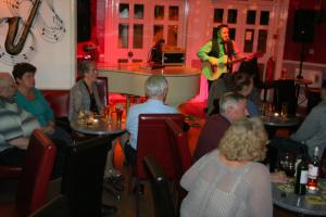 un groupe de personnes assises dans un restaurant avec un homme jouant de la guitare dans l'établissement Holliers Hotel, à Shanklin