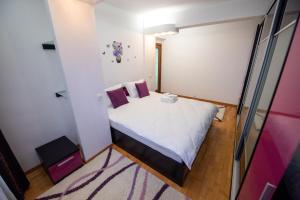een kleine slaapkamer met een wit bed met paarse kussens bij Cozy Apartment in Suceava in Suceava