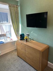 a room with a tv on the wall and a dresser at West End Guest House in Elgin