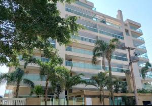 a tall building with palm trees in front of it at Apartamento a 100 metros da praia no melhor bairro de Bertioga in Bertioga