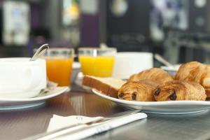 - une table avec des assiettes de viennoiseries et des tasses de jus d'orange dans l'établissement The Originals City, Hôtel La Saulaie, Saumur Ouest (Inter-Hotel), à Doué-la-Fontaine