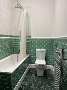 a green tiled bathroom with a toilet and a tub at Station House-Hinton Admiral in Christchurch