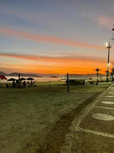 a sunset at the beach with people sitting on the grass at Apartamento frente Mar Santos in Santos