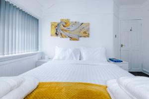 a white bedroom with a large white bed with a yellow blanket at NICE THREE BEDROOM HOUSE in Manchester in Manchester
