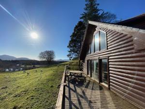 a building with a wooden deck next to a field at Great Glen Holidays - Lone Pine Lodge in Torlundy