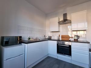 a white kitchen with white cabinets and a microwave at Granada Apartments Queen's Promenade in Blackpool