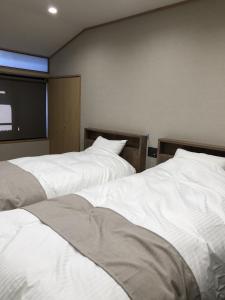 two white beds in a room with a flat screen tv at Jizokan Matsuya Ryokan in Nagano