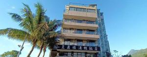 un edificio alto con un cartel junto a las palmeras en 花蓮星晟棧飯店Starry Inn近太平洋新城車站, en Xincheng