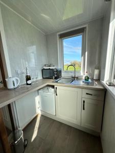Abererch的住宿－The Pod，厨房配有白色橱柜、水槽和窗户。