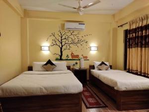 a bedroom with two beds with a tree mural on the wall at Hotel Mirage Sauraha in Sauraha