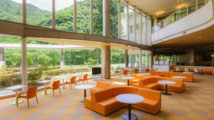 un vestíbulo con sillas naranjas, mesas y ventanas en Ooedo Onsen Monogatari Higashiyama Grand Hotel, en Aizuwakamatsu