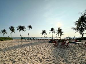 una playa de arena con mesas, sillas y palmeras en Westcoast PQ Sunshine spacious 3BR private pool villa en Phu Quoc