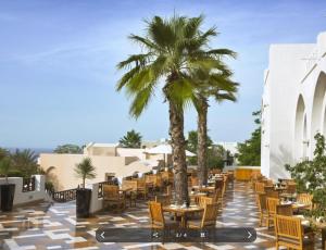 eine Terrasse mit Tischen, Stühlen und Palmen in der Unterkunft Peaceful Private Villa at Five Star Beach Resort in Ras al Khaimah