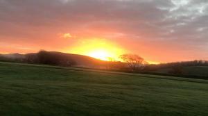 a sunset in a field with the sun setting in the background at Romantic Rural Break In Countryside Castle Grounds Private Retreat Wizards Rest in Bishops Tawton