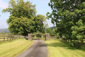 einen Eingang zu einem Zaun mit einem Tor auf einer Straße in der Unterkunft Romantic Rural Break In Countryside Castle Grounds Private Retreat Wizards Rest in Bishops Tawton