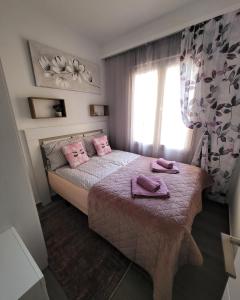 Un dormitorio con una cama con almohadas rosas y una ventana en Emma Apartman, en Santa Pola