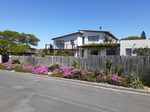 uma casa com uma cerca e flores à beira da estrada em Selkie - Two Restful Studio Apartments near Noordhoek Beach & Restaurants em Noordhoek