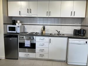 cocina con armarios blancos, fogones y microondas en 501 Sky High Cbd Style With Parkingpool en Perth