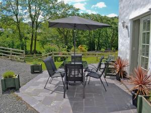 eine Terrasse mit einem Tisch, Stühlen und einem Sonnenschirm in der Unterkunft Hen Dy in Eglwys-Fâch