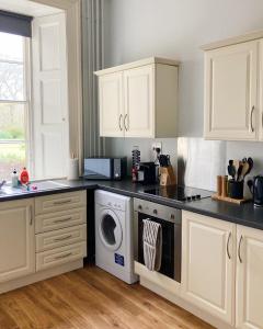 cocina con armarios blancos, lavadora y secadora en Meldon Cottage in Morpeth, Northumberland, en Morpeth