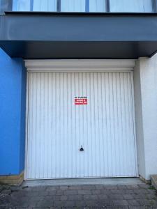 a white garage door with a red sign on it at Bluebell Cottage - private coach house, garage & parking in Greenhithe