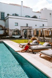 a woman laying on lounge chairs next to a swimming pool at Paragon 700 Boutique Hotel & SPA in Ostuni