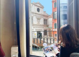 Eine Frau, die eine Zeitschrift vor einem Fenster liest. in der Unterkunft Cà dei Dalmati - the Blue Canal View in Venedig
