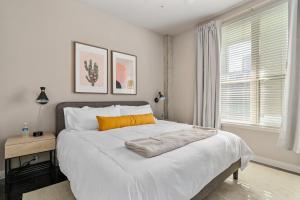 a white bedroom with a large bed with an orange pillow at Lodgeur at Elan Med Center in Houston