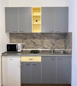 a kitchen with white cabinets and a sink and a microwave at Apartmani HILA in Njivice