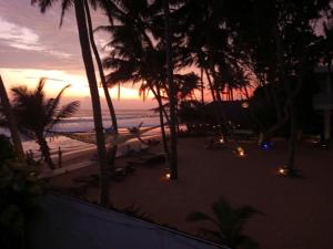 a sunset on the beach with palm trees and a hammock at Blue Ocean Villa in Hikkaduwa