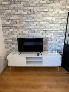 a flat screen tv on a white entertainment center in front of a brick wall at Appartement 1 chambre moderne à proximité du circuit des 24h in Le Mans