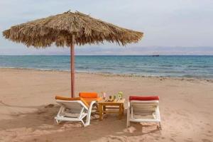 zwei Stühle und ein Tisch unter einem Sonnenschirm am Strand in der Unterkunft مصيف بلطيم 
