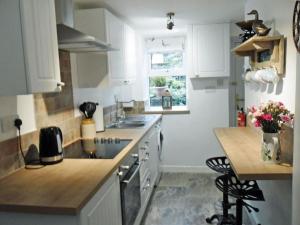 cocina con armarios blancos, fregadero y encimera en Tilly Cottage, en Greenhead