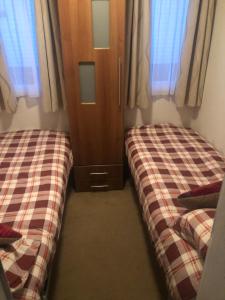 a bedroom with two beds and a cabinet and windows at First Steps Caravan Rentals in Sandown