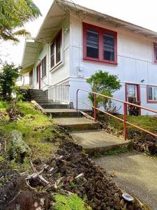 YOUR HILO HOMEBASE - Lovely 3 Bedroom in Heart of Hilo with AC! في هيلو: بيت أبيض شبابيكه حمراء ودرج له