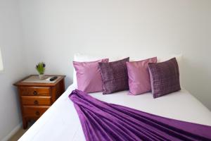 łóżko z fioletowo-białymi poduszkami i stolikiem nocnym w obiekcie BLK Stays Guest House Deluxe Units Caboolture South w mieście Caboolture