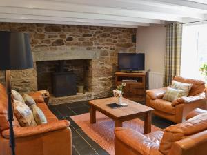a living room with leather furniture and a fireplace at Prideaux Farmhouse in Luxulyan