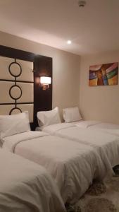 a bedroom with three beds with white sheets and a painting at فندق البيرق in Makkah
